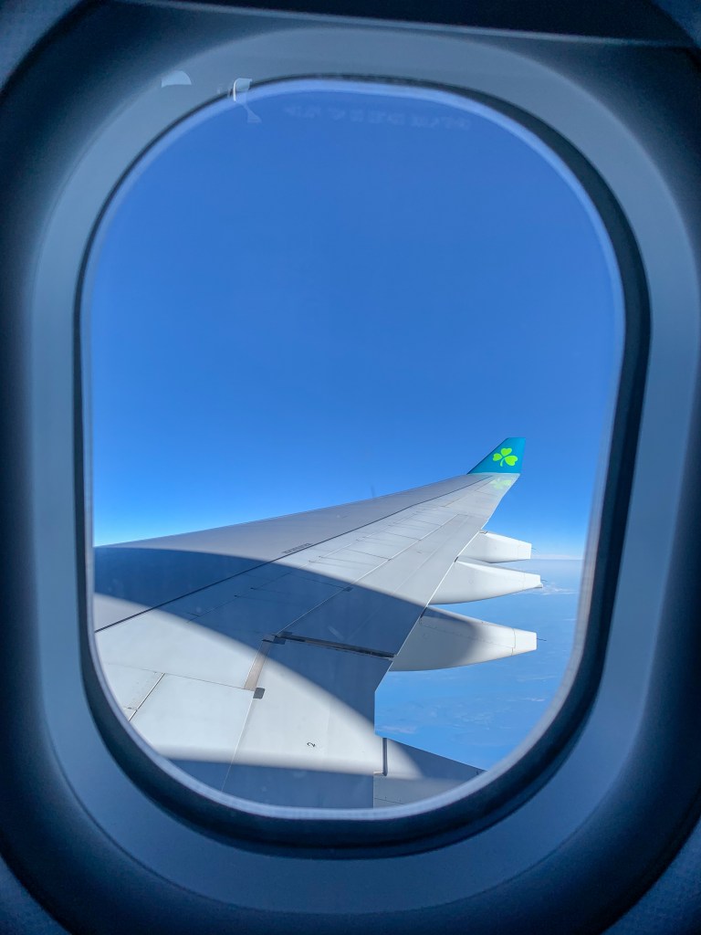 Looking out an airplane window at the wing of an airplane with a clover logo on the tip of the wing